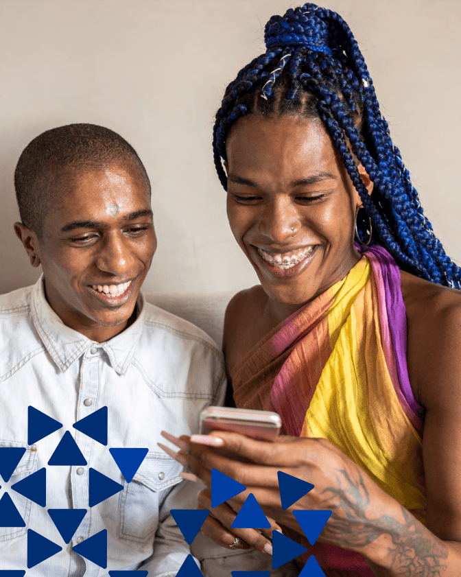 Two people looking at a phone together and smiling, one with colourful top and one with white top